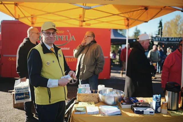 Ilkka Sillanpää keltaisessa liivissä tarjoilupöydän takana.