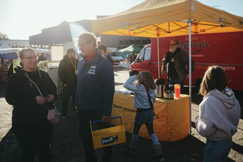 Markkinavieraita keltaisen teltan edustalla auringonpaisteessa.