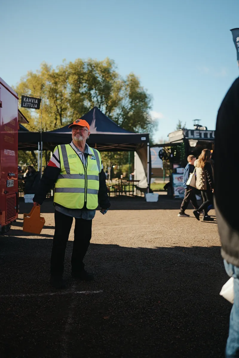 Heijastinliiviin pukeutunut markkinakävijä telttojen välisellä kulkuväylällä.